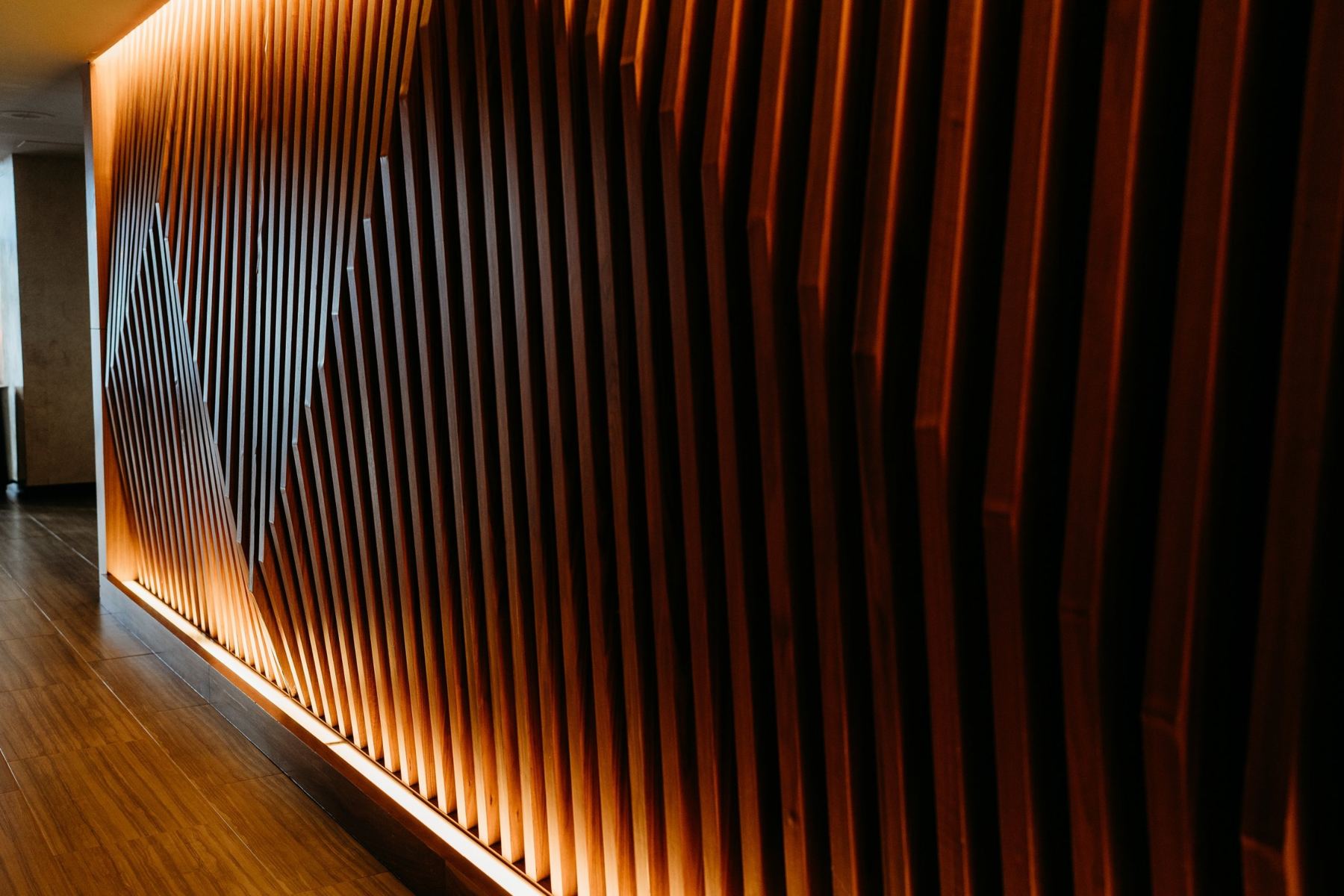 A wall of angled walnut slats lit from below with warm light.